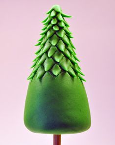 a green cake shaped like a christmas tree on top of a wooden stick in front of a pink background