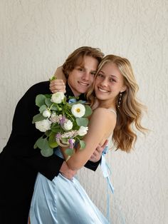 a man and woman hugging each other in front of a wall