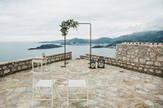 two white chairs sitting on top of a stone patio next to the ocean and mountains