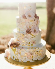 a white and gold wedding cake with pink flowers on the top tier is sitting on a table