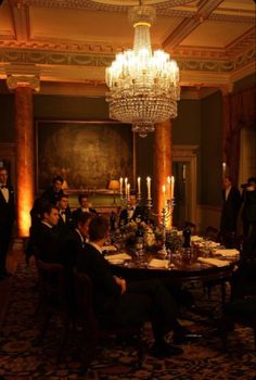 a group of people sitting around a table in a room with chandelier above it