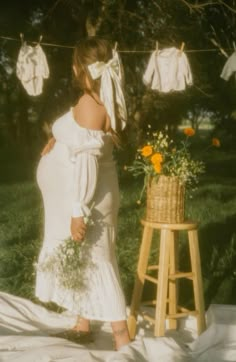 a pregnant woman is standing in front of clothes hanging on a line and holding flowers