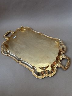 an ornately decorated gold tray with handles on a gray surface, possibly from the 19th century