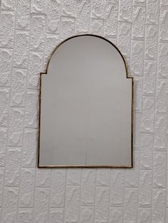 a white wall with a gold frame and mirror hanging on it's side against the wall