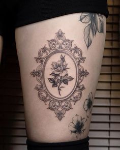 a woman's thigh with tattoos on it and flowers in the frame behind her