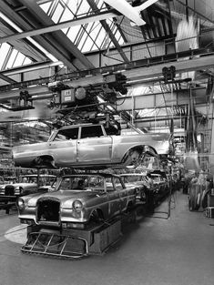 an old car is being worked on in a garage with other cars and people around it