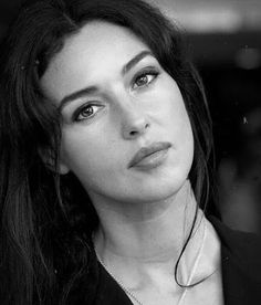 a black and white photo of a woman with long hair looking at the camera while wearing a necklace