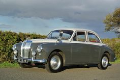 an old grey car is parked on the side of the road in front of some bushes