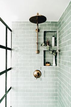 a green tiled shower with brass fixtures and shelves on the wall, along with vases