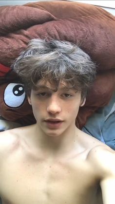 a shirtless young man laying on top of a bed next to a stuffed animal