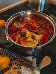 a pot filled with fruit and spices on top of a stove next to oranges