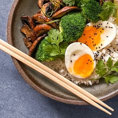 a bowl filled with rice, broccoli and eggs next to chopsticks