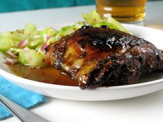 a white plate topped with meat and vegetables next to a glass of beer on a table