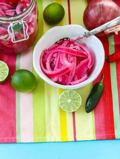 a white bowl filled with red onions next to limes and an onion pickle