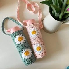 two crocheted water bottles sitting on top of a table next to a potted plant