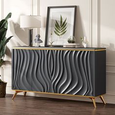 a modern sideboard with wavy design in grey and gold, next to a potted plant