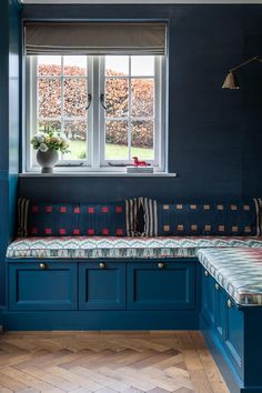 a room with blue walls and wooden flooring, two windows above the bench area