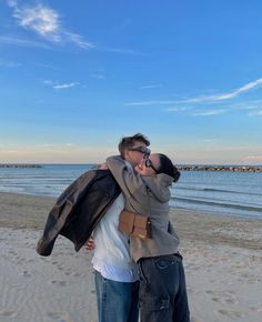 two people are hugging on the beach while talking on their cell phones and taking pictures