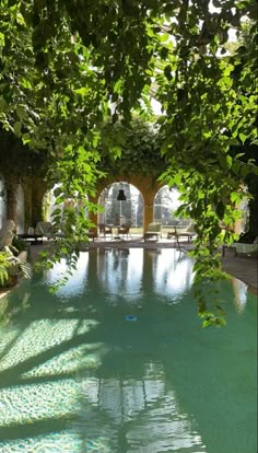 an outdoor swimming pool surrounded by greenery and stone arches with benches in the background