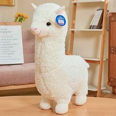 a white stuffed llama sitting on top of a wooden table next to a book shelf