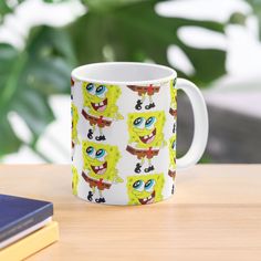 the spongebob mug is sitting next to some books and a laptop on a table