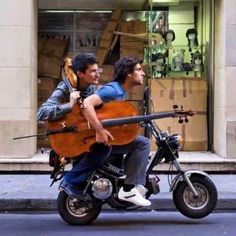 two men riding on the back of a motorcycle with an instrument strapped to it's back