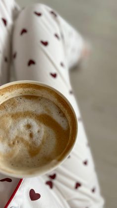 a person is holding a cup of coffee in their hand with hearts all over it