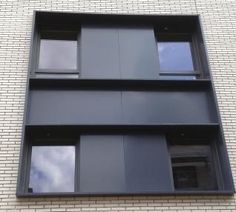 the side of a brick building with three windows on each floor and sky in the background