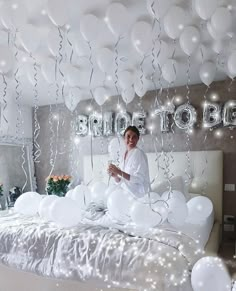 a woman is sitting on her bed surrounded by white balloons and streamers that spell out the word bride to be