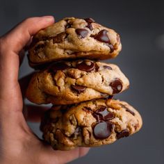 a hand holding three chocolate chip cookies on top of each other