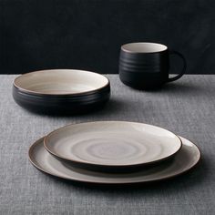 a table topped with plates and cups on top of a gray cloth covered tablecloth