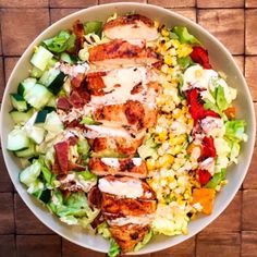 a salad with chicken, corn and dressing in a white bowl on a wooden table