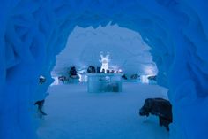 people are sitting on benches in an ice cave with snow and ice sculptures behind them