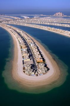 an island in the middle of water surrounded by sand and palm trees, with buildings on both sides