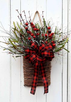 a basket filled with red berries and greenery hanging on a white wooden wall next to a door