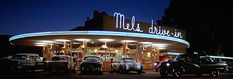 several classic cars are parked in front of a gas station at night with neon lights