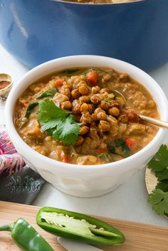 a white bowl filled with soup next to green beans and cilantro leaves on a cutting board