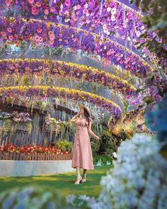 a woman in a pink dress standing under a flower covered structure with flowers all over it