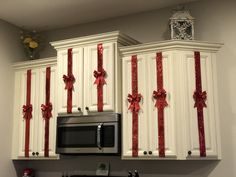 a kitchen decorated for christmas with red bows on the cabinets, microwave and stove top