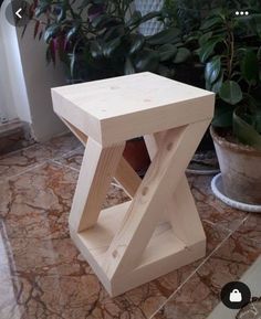 a wooden stool sitting on top of a marble floor next to a potted plant