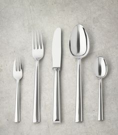 five silverware pieces are lined up in a row on a gray surface with one fork, spoon and knife