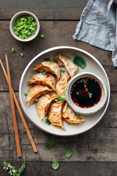 a white plate topped with dumplings next to chopsticks and a bowl of sauce