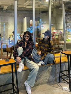 two people sitting on a bench in front of a store window, one wearing a face mask