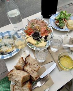 a table topped with plates of food next to glasses of water and bottles of wine