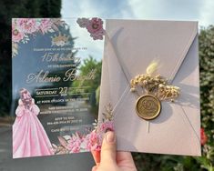 a person holding up a wedding card with flowers on it and a button attached to the front