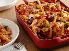 a red casserole dish filled with pasta and veggies on a wooden table