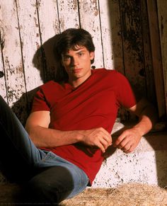 a young man sitting on the ground in front of a wooden wall