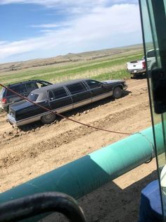 two cars parked in the middle of a dirt road near an open field with green pipes