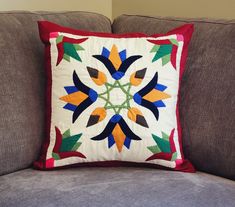 a decorative pillow sitting on top of a couch next to a gray sofa cushion with an orange, green, and blue flower design