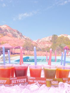 three cups filled with orange juice sitting on top of ice next to a swimming pool